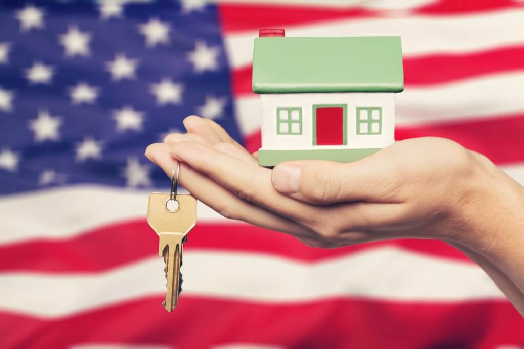 Hand holding a model of house and key on the USA flag background